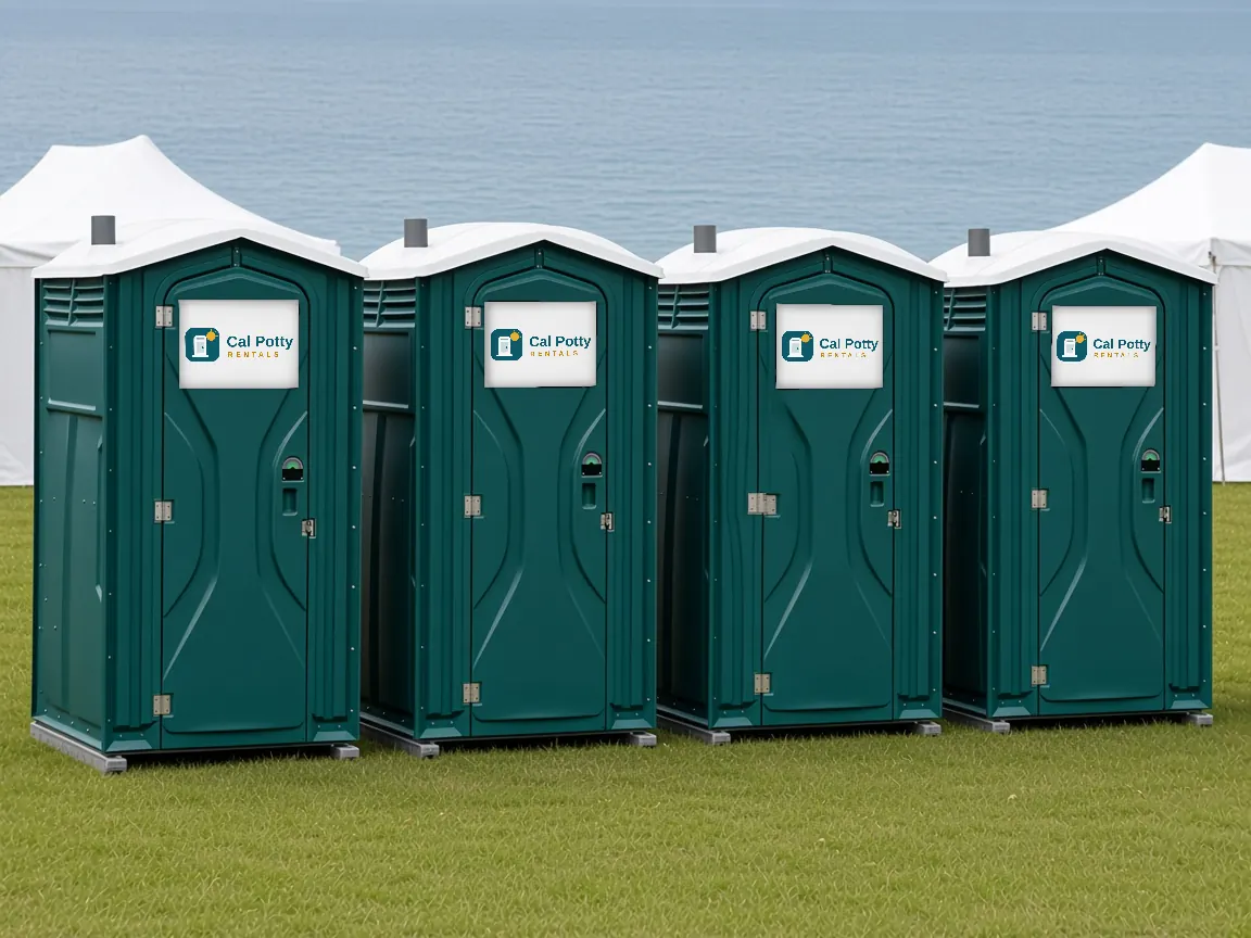 Four teal portable toilets on a lawn at an outdoor event with white tents behind