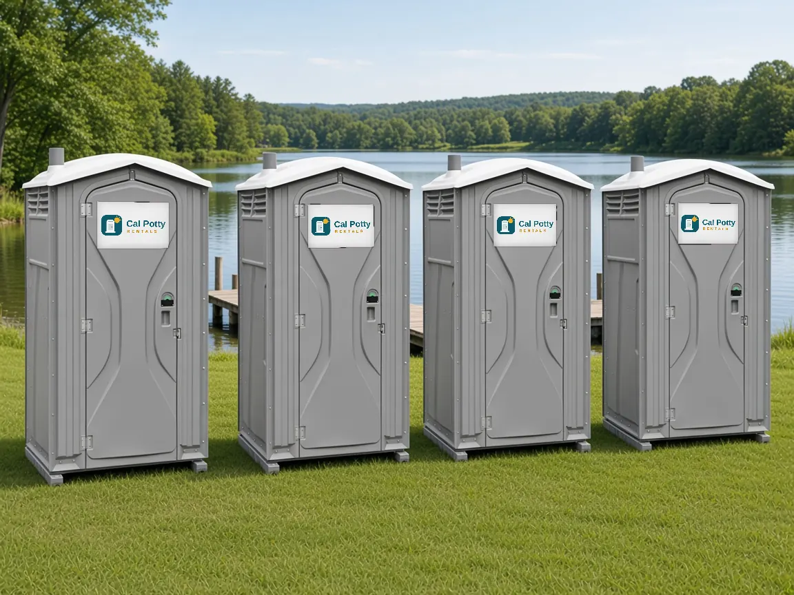 Four grey porta potties in a row on a lakeside lawn, an example setup for porta potty rental in Los Altos
