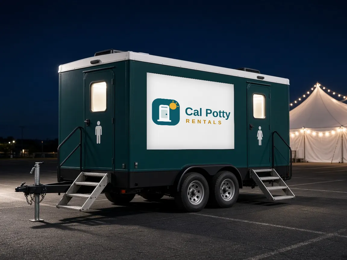 A teal restroom trailer at night in a parking lot with a lit white tent behind